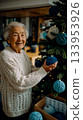 An older woman decorating a Christmas tree with blue ornaments 133953926