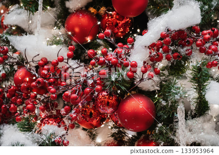 Red berries and ornaments on snowy Christmas tree with warm lights and festive classic holiday decor. 133953964