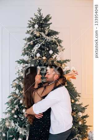Couple celebrating under a beautifully decorated Christmas tree in a cozy room full of festive spirit and joy 133954048