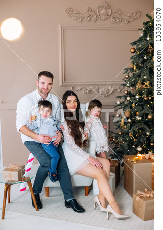 Family gathering near Christmas tree with presents and decorations while celebrating the festive season 133954070