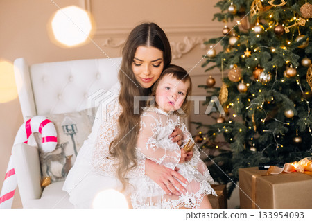 Mother and child share a cozy moment by decorated Christmas tree in warm living room setting during holiday season Mother and child share a cozy moment by decorated Christmas tree in warm living room setting during holiday season 133954093