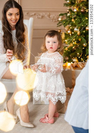 Warm holiday gathering with a young child and adult by the Christmas tree in a cozy living room during winter festivities 133954102