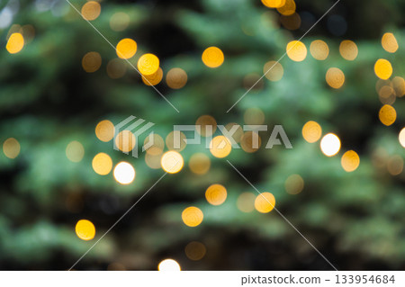Blurred Christmas tree with golden lights garland. Abstract pattern. Defocused background. Xmas holiday spirit. 133954684