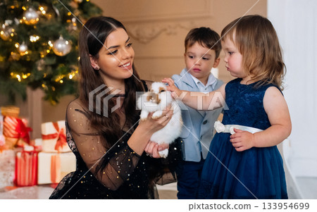 Family celebration with children and a rabbit during a festive holiday season in a cozy home decorated with lights and gifts 133954699