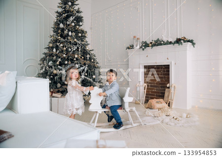 Kids playing in a bright room decorated for the holidays with a Christmas tree and cozy fireplace during winter 133954853