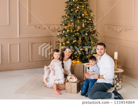 Family celebrating holiday moments together near decorated Christmas tree indoors with gifts and festive decor 133954864