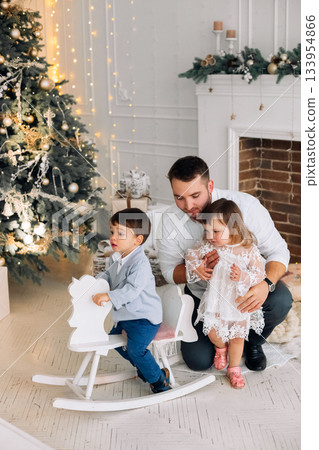 Children enjoy holiday spirit while playing with a rocking horse near a festive Christmas tree and warm fireplace in a cozy home setting during winter 133954866