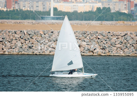 Russia, St. Petersburg, The sports sailing dinghy is heeling at sunny day, athletes tilt the boat, speed and spray, reflection of sun on water surface Russia, St. Petersburg, The sports sailing dinghy is heeling at sunny day, athletes tilt the boat, speed and spray, reflection of sun on water surface 133955095