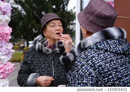 an adult elderly woman on the street in a hat and coat in front of a mirror an adult elderly woman on the street in a hat and coat in front of a mirror 133955423