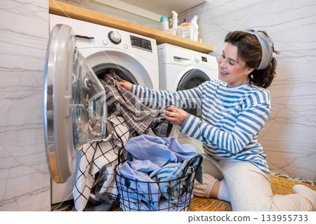 Modern housewife putting dirty linen textile and clothes to washing machine at domestic laundry 133955733