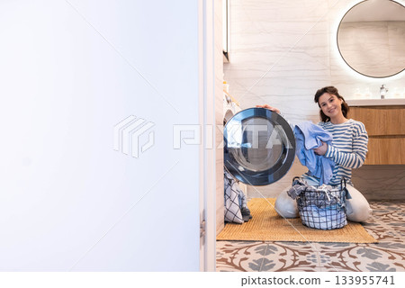 Smiling woman housewife cleaning linen textile clothes putting washing machine and dryer at laundry 133955741