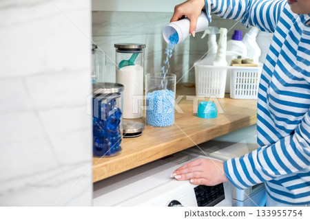 Female housewife hands sprinkle dry blue granular laundry conditioner glass can storage organizing 133955754