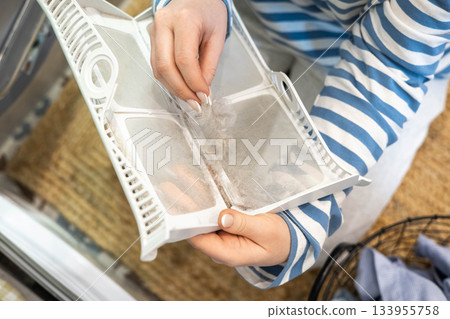 Female housewife hands cleaning filter dryer machine from wool textile fiber and particles closeup Female housewife hands cleaning filter dryer machine from wool textile fiber and particles closeup 133955758