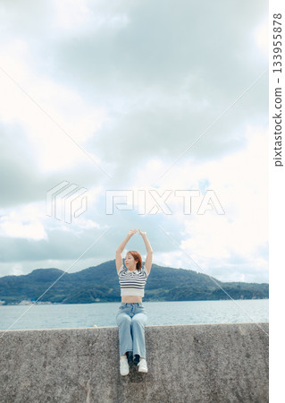 A woman in her twenties spreads her arms out to the sea. An emotional moment of freedom and liberation felt on a trip. 133955878