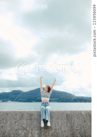 二十多歲的女子手持智慧型手機，背景是蔚藍的大海。這是旅行途中捕捉美好回憶的動人瞬間。 133956094