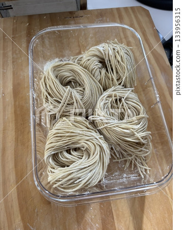Homemade noodles with slightly uneven strands, soft golden texture, and rustic appearance, served freshly cooked to highlight their warmth, smooth surface, and authentic handmade 133956315