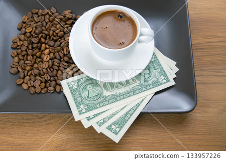 Hot espresso in a white ceramic cup placed on a saucer, next to scattered coffee beans 133957226