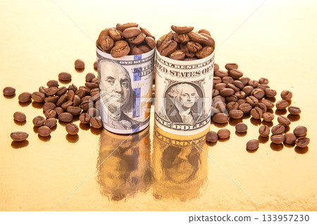 Coffee beans spill from a rolled U.S. dollar bill on a reflective gold backdrop 133957230