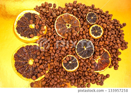 Dried orange slices rest atop a pile of roasted coffee beans on a golden surface 133957258