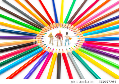 Three figurines are encircled by a spectrum of colored pencils, arranged in a starburst pattern 133957264