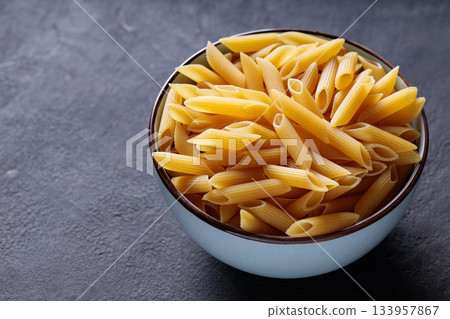 Uncooked Penne Pasta in Bowl on Dark Stone Background Copy Space Uncooked Penne Pasta in Bowl on Dark Stone Background Copy Space 133957867