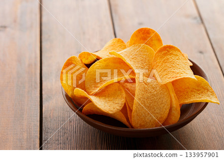 Golden Crispy Potato Chips in Bowl on Wooden Table Close-Up Golden Crispy Potato Chips in Bowl on Wooden Table Close-Up 133957901