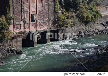 A landscape with a fast-flowing river, brick buildings and trees 133959694