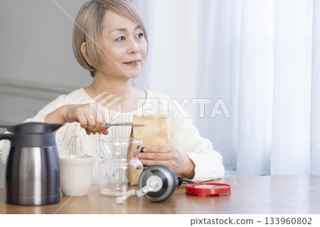 A senior woman relaxing in the living room, grinding coffee beans and drinking coffee 133960802