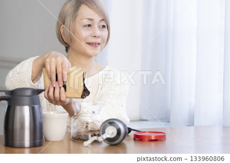 A senior woman relaxing in the living room, grinding coffee beans and drinking coffee 133960806