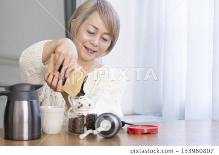 A senior woman relaxing in the living room, grinding coffee beans and drinking coffee 133960807