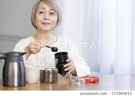 A senior woman relaxing in the living room, grinding coffee beans and drinking coffee A senior woman relaxing in the living room, grinding coffee beans and drinking coffee 133960813