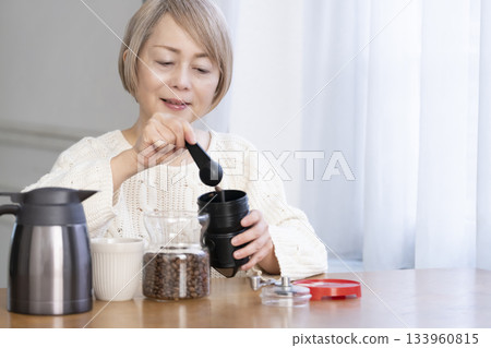 A senior woman relaxing in the living room, grinding coffee beans and drinking coffee A senior woman relaxing in the living room, grinding coffee beans and drinking coffee 133960815