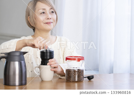 A senior woman relaxing in the living room, grinding coffee beans and drinking coffee 133960816