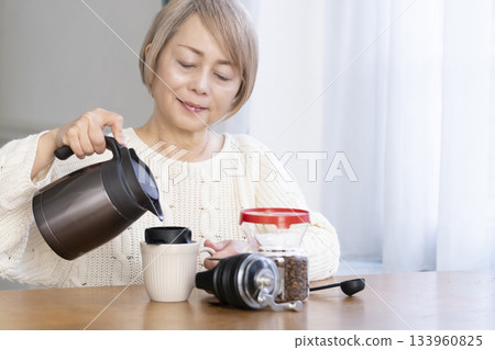A senior woman relaxing in the living room, grinding coffee beans and drinking coffee 133960825