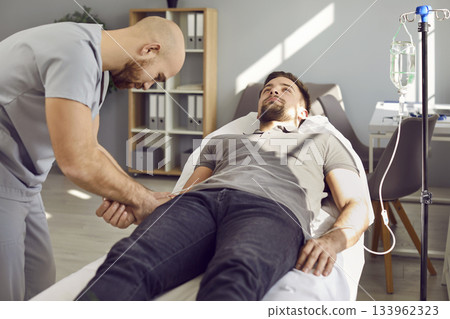 Nurse puts intravenous vitamin infusion catheter in vein of young male patient on bed Nurse puts intravenous vitamin infusion catheter in vein of young male patient on bed 133962323