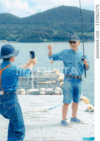 一對老年夫婦正在為他們釣到的魚拍紀念照。 133962378