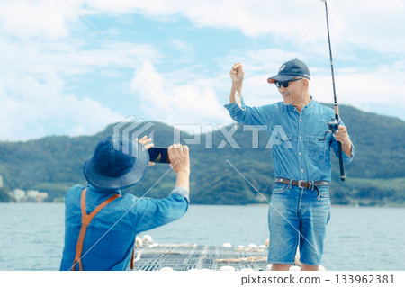 Senior couple taking a commemorative photo of the fish they caught 133962381