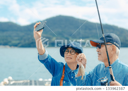 一對老年夫婦正在為他們釣到的魚拍紀念照。 133962387