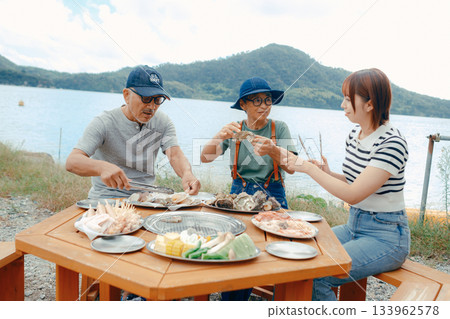 A scene of three parents and children enjoying a BBQ by the lake A scene of three parents and children enjoying a BBQ by the lake 133962578