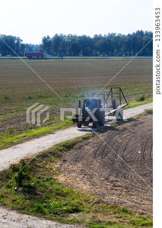 Harvester prepares postharvest cleanup, Lone tractor crosses stubbled land at sunset 133963453