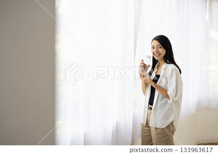 一位微笑的女子在窗邊喝水。 133963617