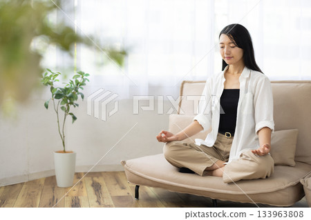 一位女子閉著眼睛，在沙發上冥想。 133963808