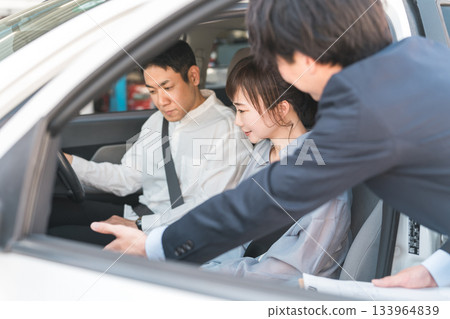 一位年輕的亞裔男性推銷員為前來選購、估價、購車的顧客服務。 一位年輕的亞裔男性推銷員為前來選購、估價、購車的顧客服務。 133964839