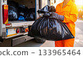 Garbage collector handling waste bag near truck at sunset 133965464