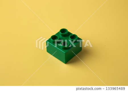 Green plastic building toy block on yellow background 133965489