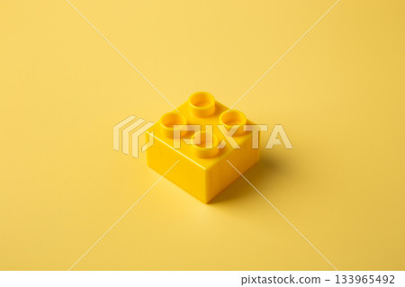 Yellow plastic toy block on monochrome background Yellow plastic toy block on monochrome background 133965492