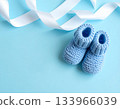 Blue knitted baby booties and white ribbon on pastel background 133966039