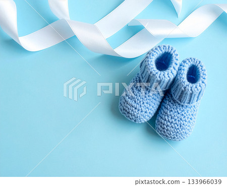 Blue knitted baby booties and white ribbon on pastel background 133966039