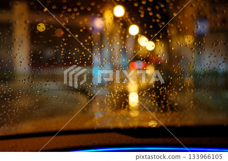 Rain drops on car windshield at night with city lights bokeh. Rain drops on car windshield at night with city lights bokeh. 133966105