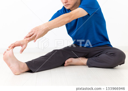 A middle-aged man in a T-shirt doing leg stretching exercises A middle-aged man in a T-shirt doing leg stretching exercises 133966946